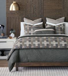 a bed with grey and white comforter next to a wooden headboard in a bedroom