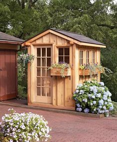 a wooden shed with windows and flowers in the front yard on a brick patio area