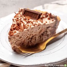 a piece of cake on a white plate with a gold fork and chocolate bar in the middle