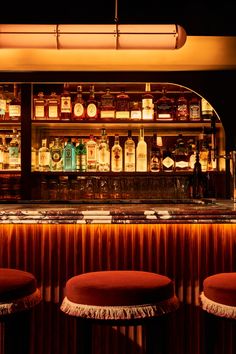 the bar has three stools in front of it and many bottles on the shelves