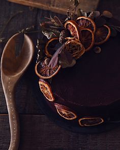 a chocolate cake with dried oranges on top and a wooden spoon next to it