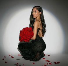 a woman kneeling down holding a bunch of red roses in her hand and looking at the camera