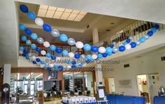 blue and white balloons are hanging from the ceiling in an open area with tables and chairs