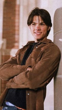 a young man leaning against a wall with his arms crossed