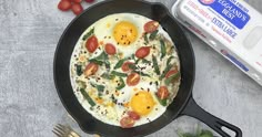 eggs and tomatoes in a skillet on a table next to an egg carton