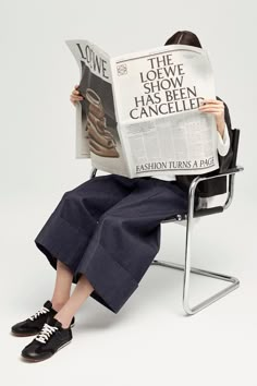 a woman sitting in a chair while reading a paper with the same image on it