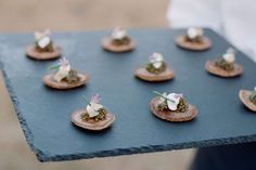 small appetizers are arranged on a slate platter, with tiny flowers in the center