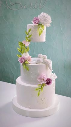 three tiered wedding cake with pink and white flowers on the top, sitting on a table