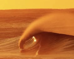 a large wave is coming in to the shore at sunset or sunrise, as seen from behind