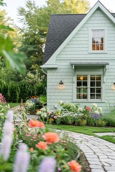 a blue house with white windows surrounded by flowers and greenery in the front yard