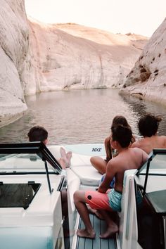 three people are sitting on the back of a boat in the water near some cliffs