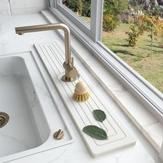 a white sink sitting under a window next to a green leafy plant on the counter