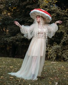 a woman in a white dress and red hat with her arms out, standing on the grass