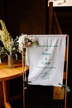 a wedding sign on a chair with flowers and greenery in vases next to it