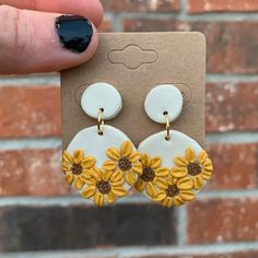 a person holding up a pair of yellow and white earrings with sunflowers on them