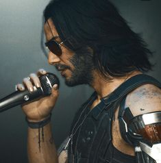 a man with long hair holding a microphone in his right hand and wearing metal gear