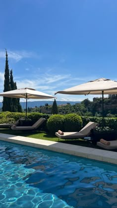 an outdoor swimming pool with lounge chairs and umbrellas on the lawn next to it