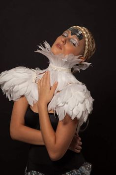 a woman with white feathers on her head and chest, posing for the camera in front of a black background