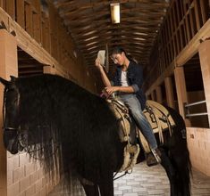 a woman riding on the back of a black horse in a barn next to a brick wall