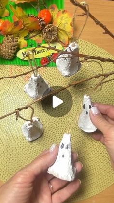 two hands are holding small white rocks on a table with autumn decorations in the background