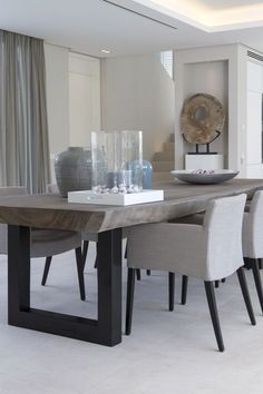 a dining room table with chairs and vases on it in front of a window