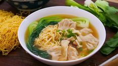 a bowl of soup with noodles, meat and vegetables on a wooden table next to chopsticks