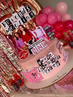 a cake with pink frosting and pictures on it sitting in front of some balloons