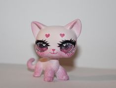 a small pink cat with big eyes and hearts on it's face, sitting on a table