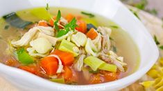 a white bowl filled with chicken and vegetable soup on top of a wooden cutting board