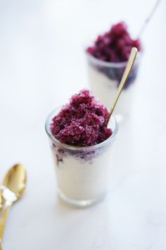 two small cups filled with food on top of a white table next to gold spoons