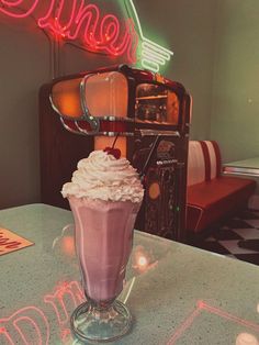 a pink drink sitting on top of a table in front of a neon light sign