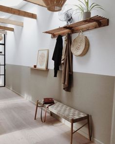 a room with a bench, coat rack and potted plant on the wall next to it