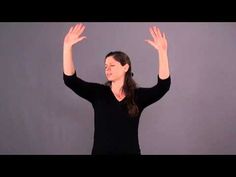 a woman with her hands up in the air while standing against a gray background and wearing a black shirt