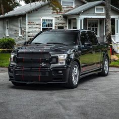 a black truck is parked in front of a house with red stripes on the hood