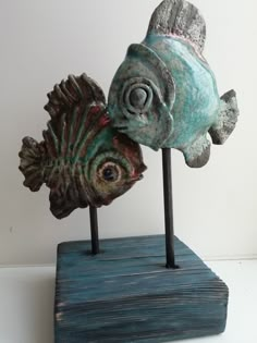 two metal fish on wooden stand with white wall in background