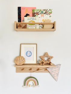 two wooden shelves holding books and toys on top of a white wall next to a rainbow ornament