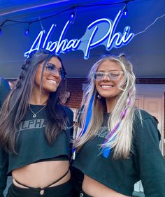 two beautiful women standing next to each other in front of a neon sign