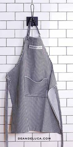 an apron hanging on the wall in front of a white brick wall with black and white stripes