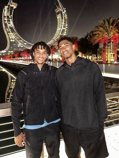 two young men standing next to each other in front of a ferris wheel at night