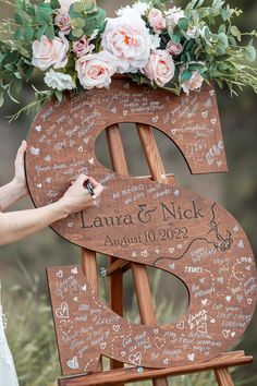 a wooden sign with writing on it and flowers in the top, is being held up by a woman