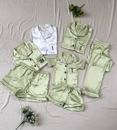 five pieces of green and white clothing laid out on top of a bed next to flowers