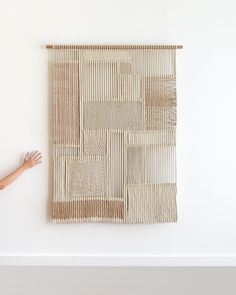 a woman standing in front of a woven wall hanging