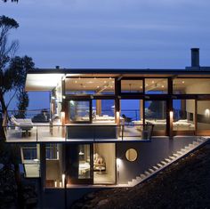 a modern house is lit up at night with lights on the balcony and stairs leading to the upper level