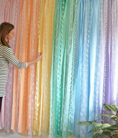 a woman standing next to a rainbow colored curtain