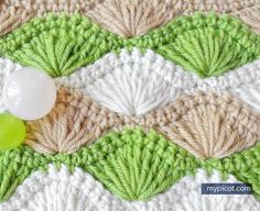 a crocheted blanket with green and white yarn on it, next to a plastic bottle