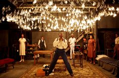 a group of people standing in a room with lights hanging from the ceiling above them