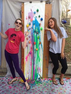 two girls standing next to an art piece with paint splattered all over it