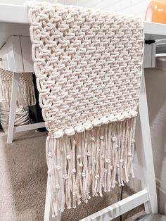 a white table with a crocheted blanket hanging from it's side, on top of a carpeted floor