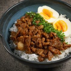 a bowl filled with rice and meat on top of a table next to an egg