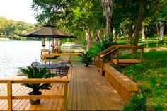 a wooden deck with chairs and an umbrella on it next to the water in a park